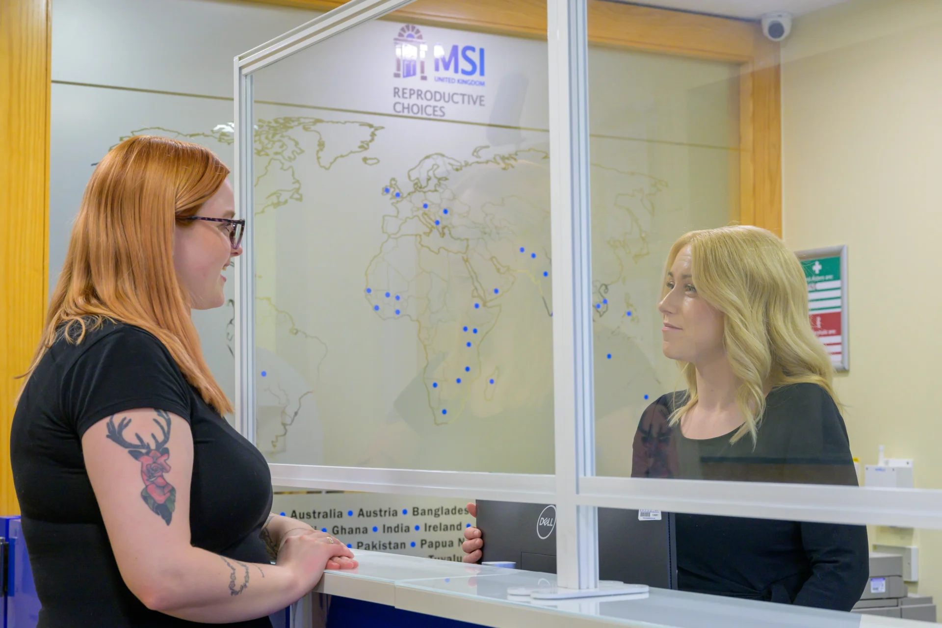A client stood at the reception desk of a clinic, speaking to the receptionist.