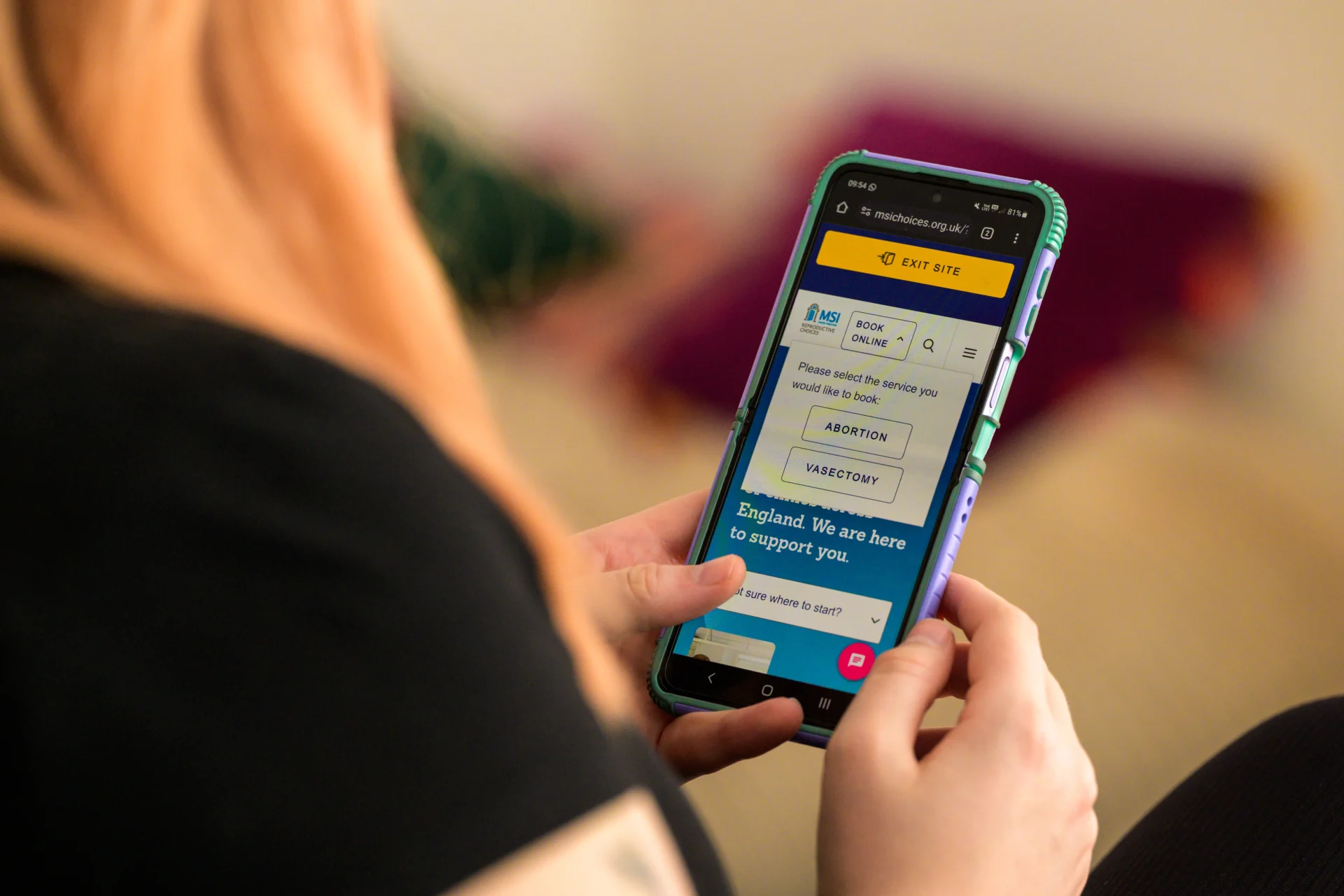A person holding their phone and scrolling on the MSI UK mobile site. They have clicked on the dropdown menu for 'book online'.